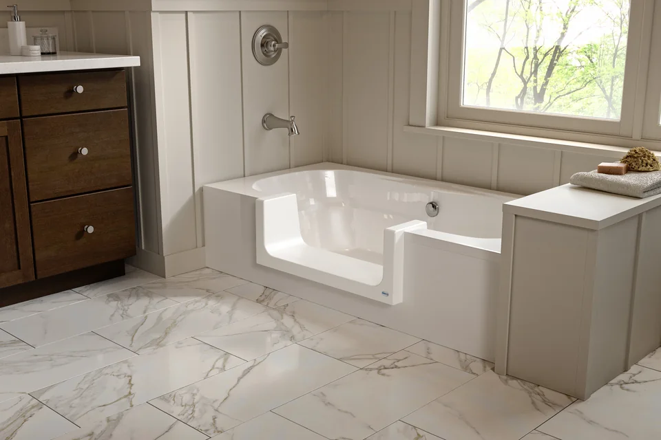 White bathtub with a fitted step-through opening beside a wood vanity and a bright window.
